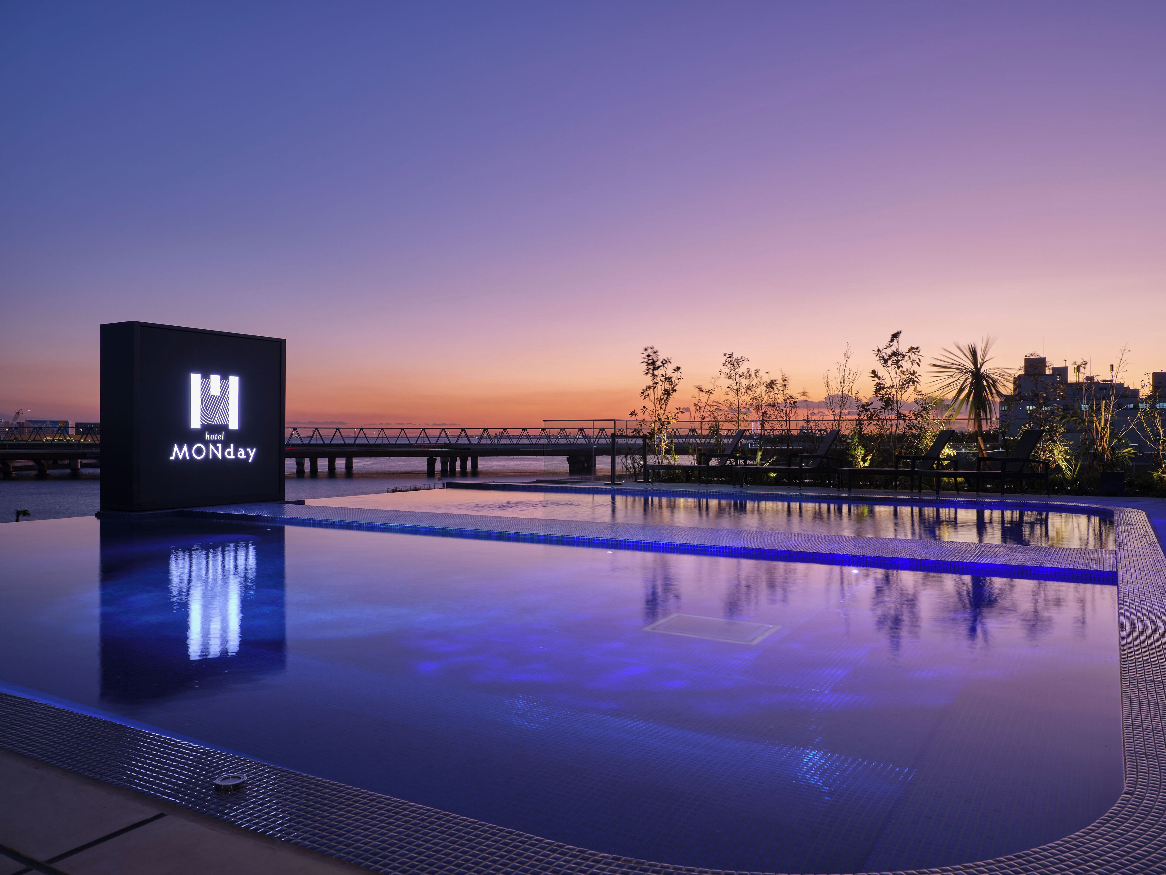 A pool area with a sign reading "hotel MONDAY" and a city skyline in the background.