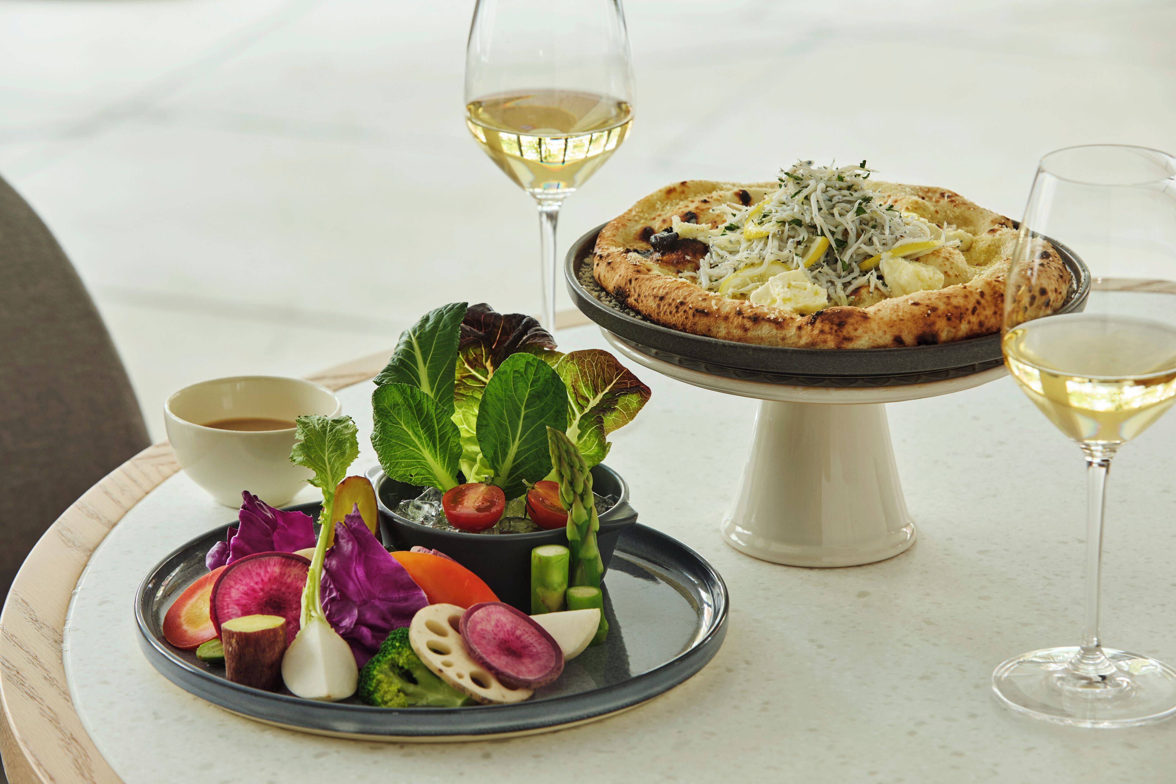 Une table à manger avec une pizza, une salade et deux verres de vin blanc.