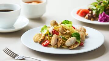 Um prato de massa com amêijoas e legumes, um garfo e duas tigelas de molho em uma mesa.