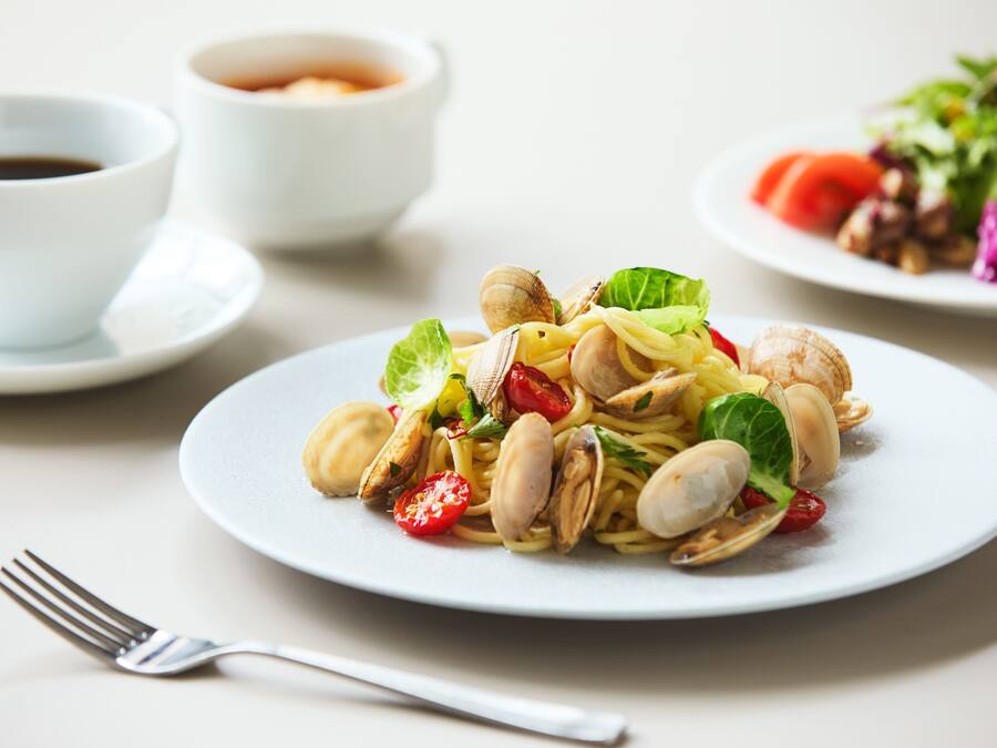 Um prato de massa com amêijoas e legumes, um garfo e duas tigelas de molho em uma mesa.