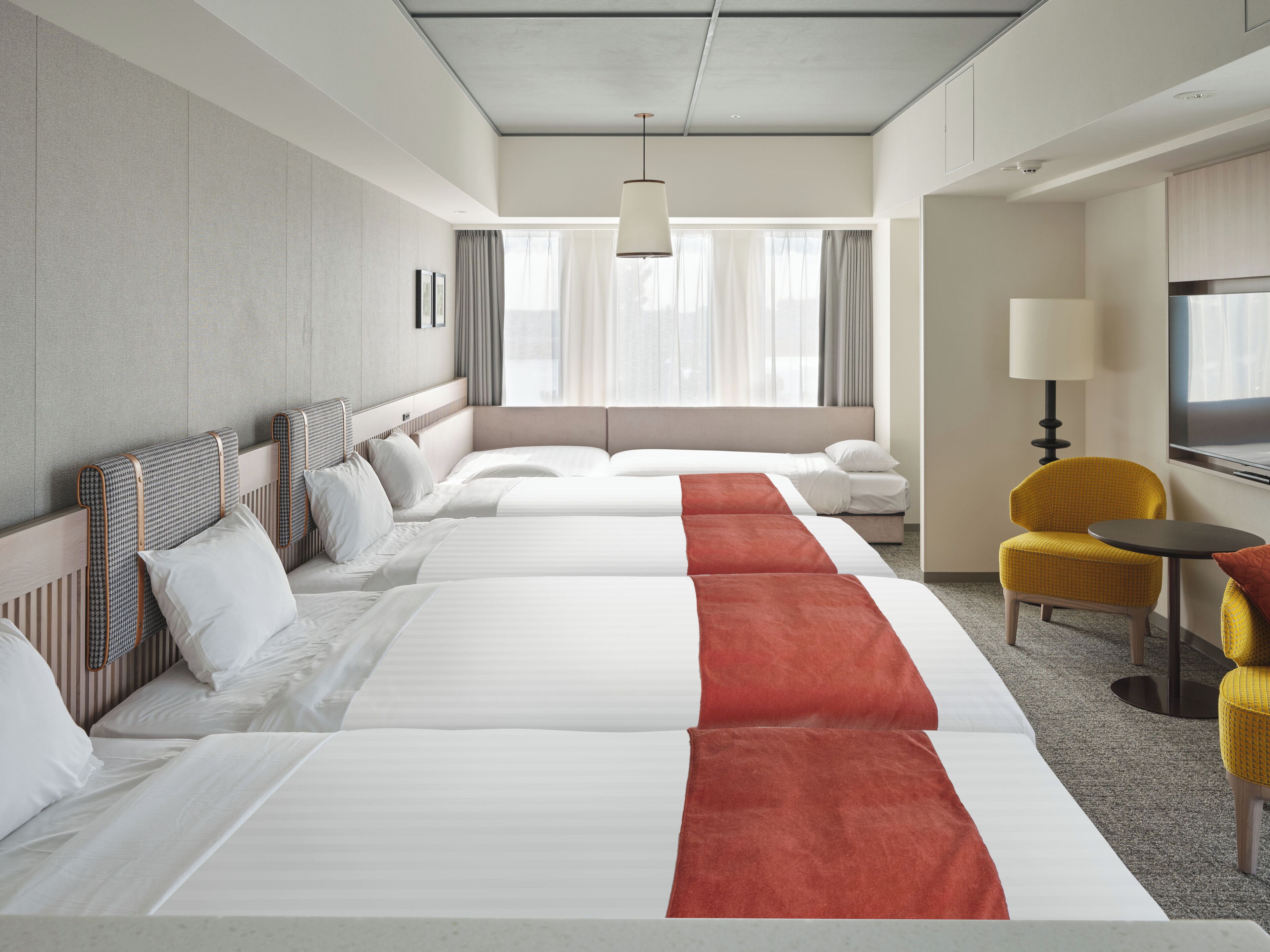 A hotel room with three beds, a sofa, a TV, and a small table.