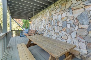 A wooden deck with a stone wall backdrop, a picnic table, and a blue chair. - Decks + Lake Access: Scenic North Carolina Retreat (Old Fort)