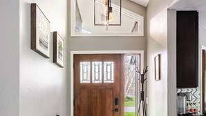 A hallway with a wooden door, a standing lamp, a patterned rug, and a small table with a plant. - Spacious 5-bedroom house in North Spokane with Hot tub & game room. (Spokane)