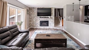 A living room with a fireplace, a sofa, a coffee table, and a TV mounted on the wall. - Spacious 5-bedroom house in North Spokane with Hot tub & game room. (Spokane)
