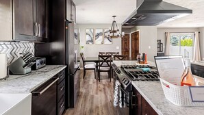 A modern kitchen with dark cabinetry, a marble countertop, a dining area with a table and chairs, and a view of greenery outside. - Spacious 5-bedroom house in North Spokane with Hot tub & game room. (Spokane)