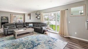A living room with a sectional sofa, a coffee table, and a large window with curtains. - Spacious 5-bedroom house in North Spokane with Hot tub & game room. (Spokane)