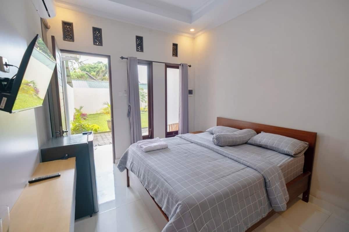 A bedroom with a bed, a desk, and a TV. There are sliding doors leading to an outdoor area.