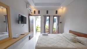 Un dormitorio con una cama grande, un televisor montado en la pared, un baño con espejo y un ventanal corredero que da a un balcón.