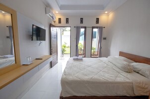 Un dormitorio con una cama grande, un televisor montado en la pared, un baño con espejo y un ventanal corredero que da a un balcón.