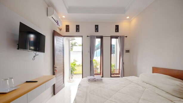 Un dormitorio con cama, televisor montado en la pared, mesita de noche de madera y puerta que da a un balcón.
