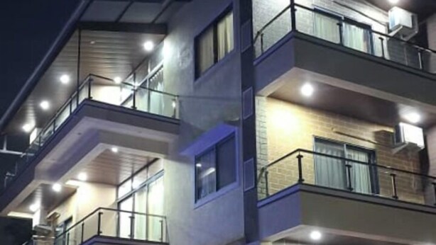 Un edifici de diversos pisos amb balcons, grans finestres i una zona d'entrada pavimentada.