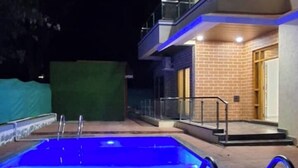 Una piscina de disseny modern, envoltada d'un camí de pedra i un edifici de diverses plantes amb baranes de vidre.