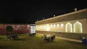 Un espace extérieur aménagé avec des tables et des chaises, un mur agrémenté d’un éclairage décoratif et, au fond, un mur en briques.
