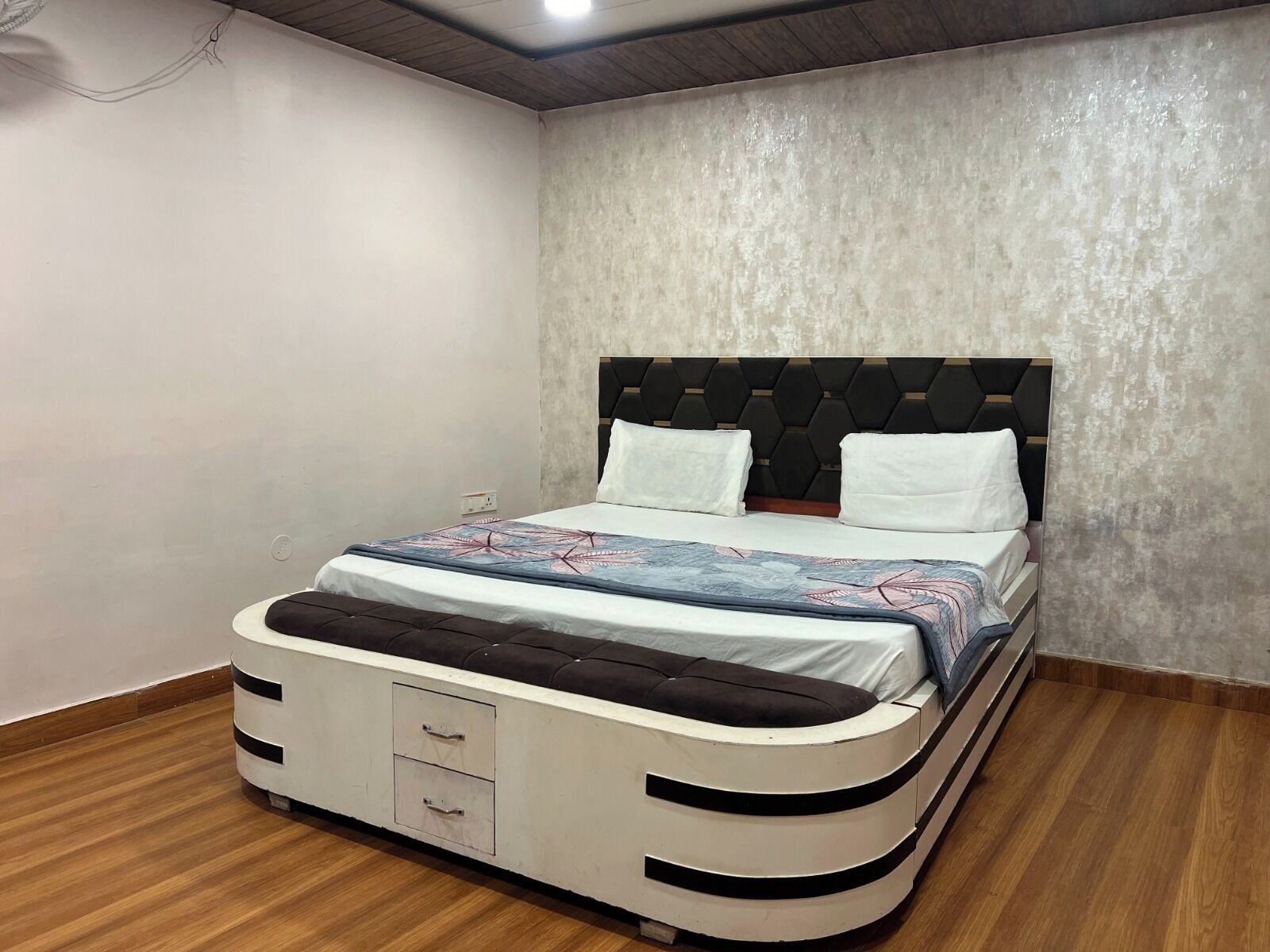 A bed with a headboard, a bedside table with drawers, and a wall with a textured finish.