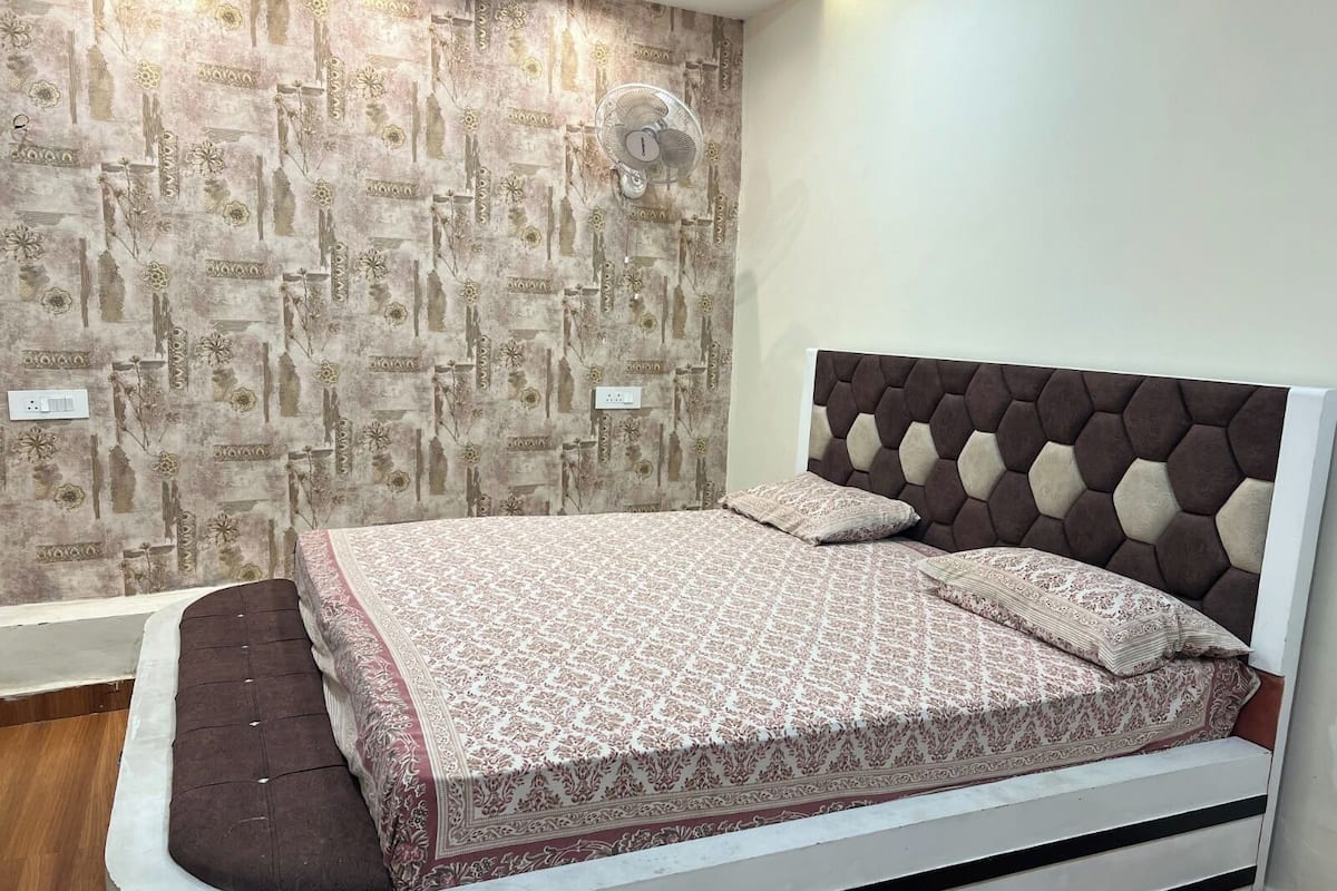 Un dormitorio con pared estampada, una cama con cabecera capitonada y una mesita de noche.