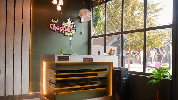 Un comptoir d'accueil avec un panneau lumineux au néon, un ventilateur et une vue sur l'extérieur par la fenêtre.