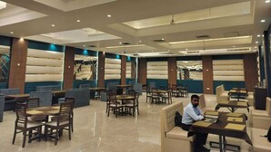 Un hall d’hôtel spacieux, doté de plusieurs espaces de détente, notamment des canapés et des tables, ainsi que d’un lustre moderne.