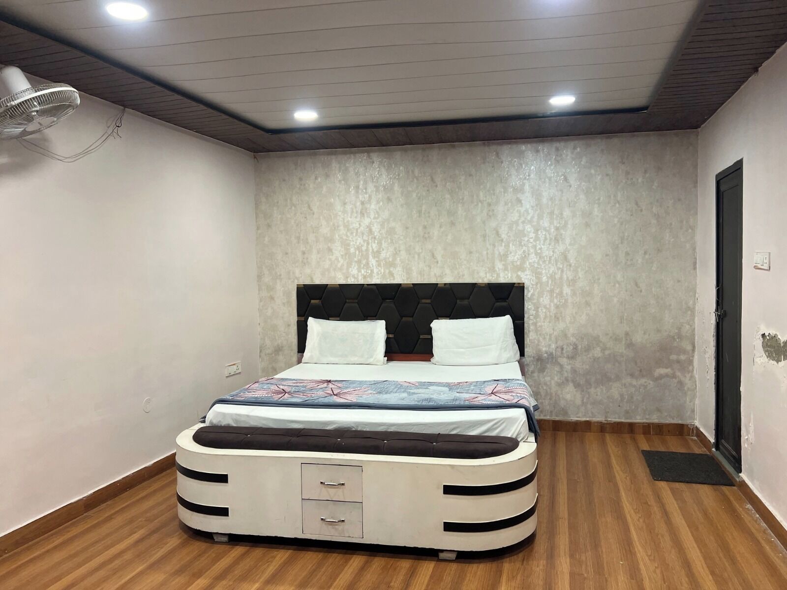 A bedroom with a bed, a ceiling fan, and a wooden floor.