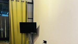 Une pièce avec un canapé rouge, un rideau jaune, un téléviseur à écran plat fixé au mur et un plancher en bois.