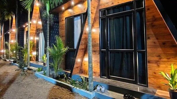 Une rangée de chalets de style « A », dotés de grandes fenêtres et d’une façade en bois, entourés de palmiers et de plantes en pot.