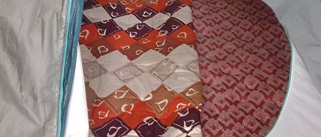 A tent with a quilted bedspread inside.