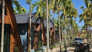 Un bâtiment moderne doté d’un toit triangulaire au design original, entouré de palmiers et avec une moto garée à proximité.