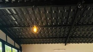 Un salon moderne avec un canapé gris, un pouf marron et un luminaire suspendu.