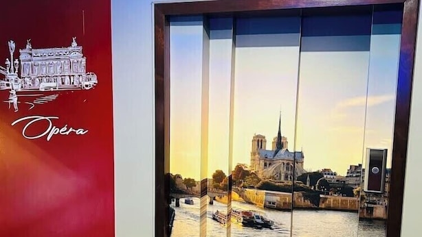 A hotel room with a red wall, a patterned carpet, and a large window with a view of a river and a building. - Hotel le Paris (Nouméa)