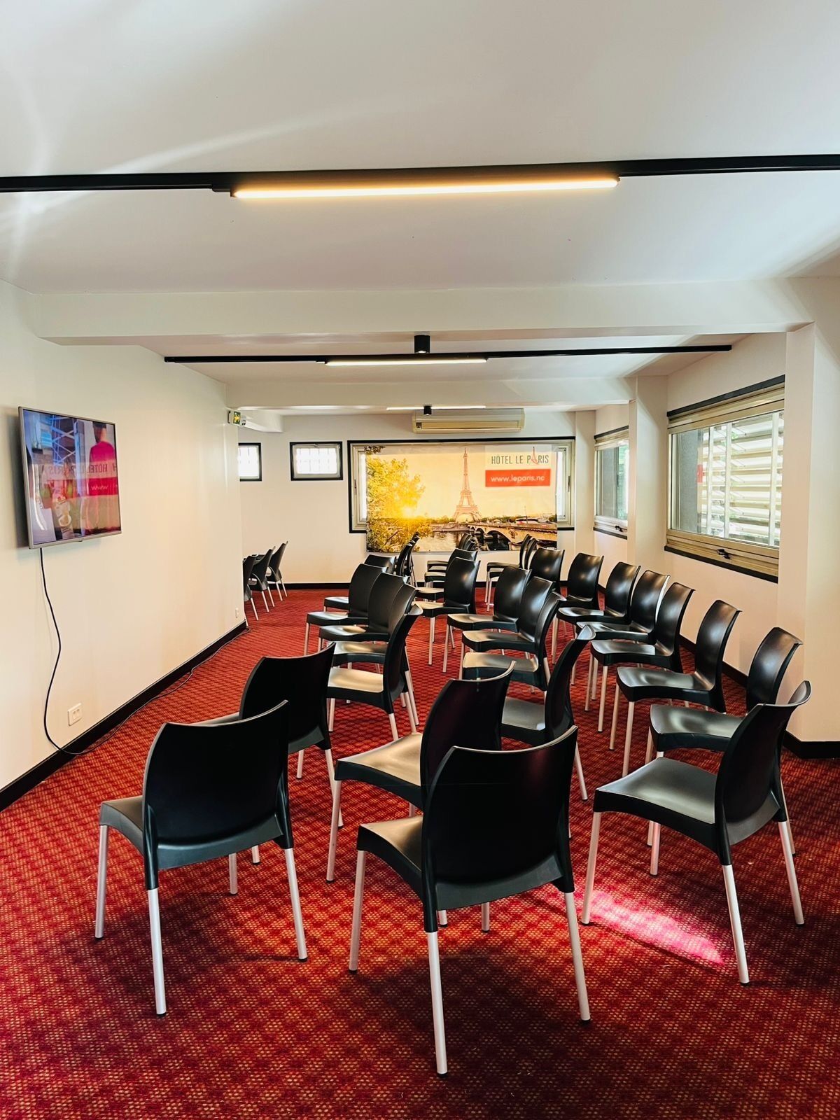 A conference room with rows of black chairs, a red carpet, a large poster of the Eiffel Tower, and a television on the wall.