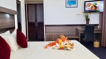 Une chambre d’hôtel comprenant un lit, une table à manger avec un plateau de petit-déjeuner, une télévision et un bureau.