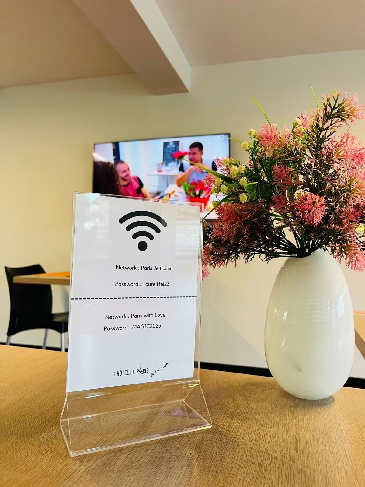 A hotel sign with network and password information, a vase with flowers, and a television in the background.