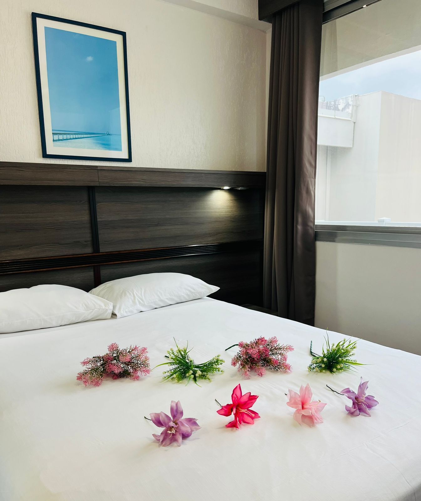 A hotel room with a neatly made bed, a framed picture on the wall, and a window with curtains.