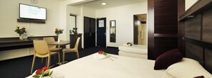 A hotel room with a bed, a desk, and a chair. There is a clock on the wall and a TV mounted above the desk. - Hotel le Paris (Nouméa)