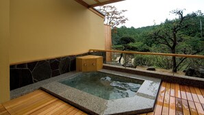 Una terraza de madera con hidromasaje y paredes de piedra, con vistas a un área boscosa.