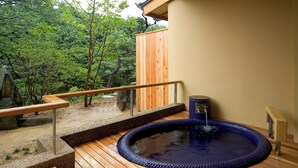 Un área de aguas termales con una terraza de madera, una bañera de hidromasaje y una pila de piedra.