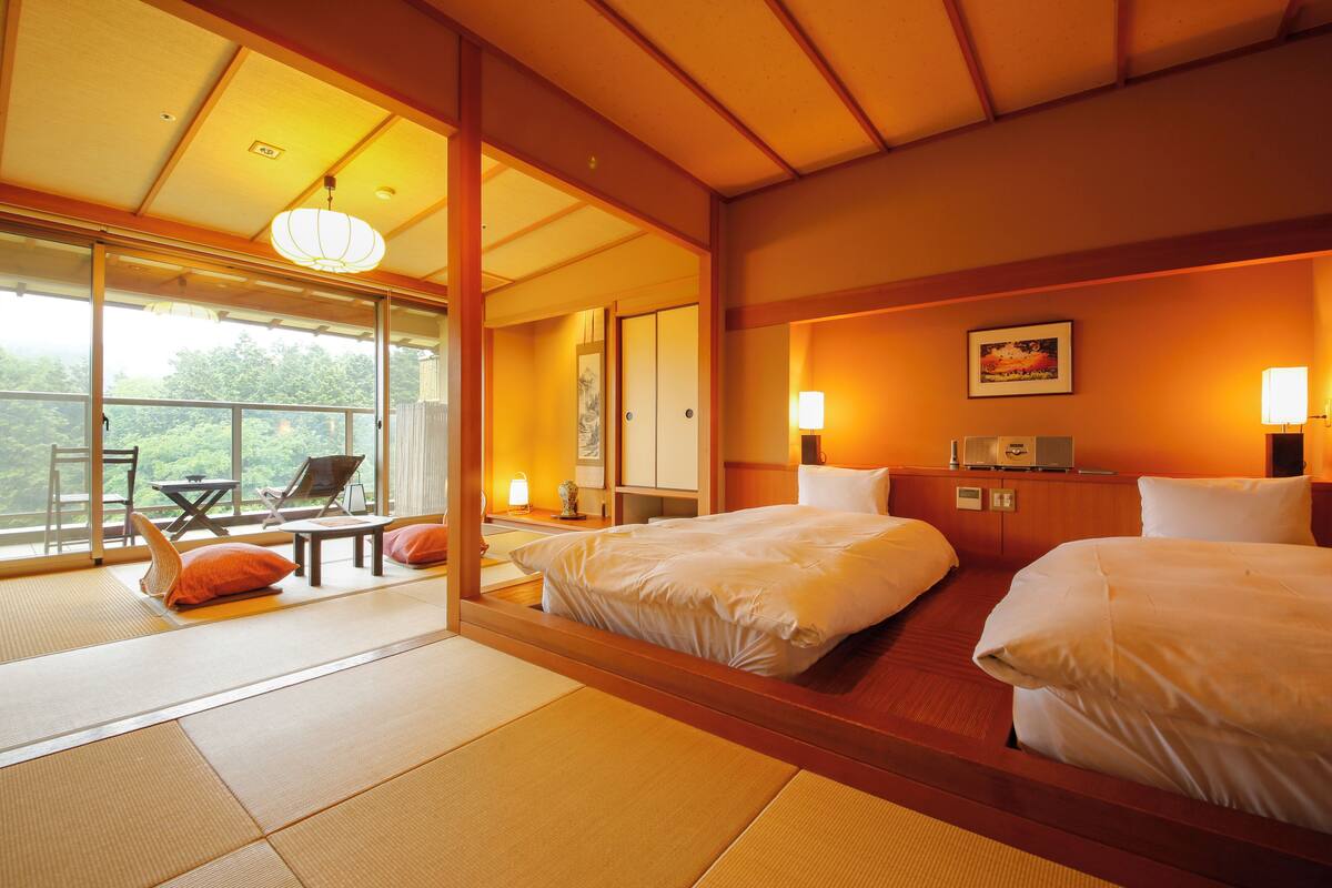 A hotel room with tatami mats, a bed, a desk, and a view of the outdoors.