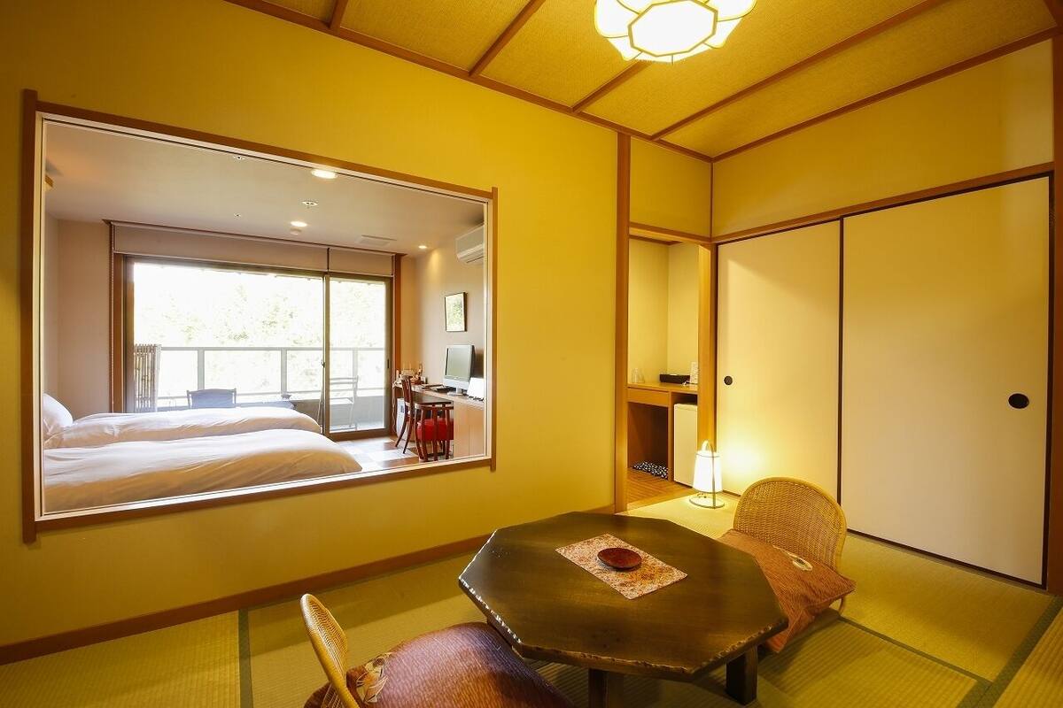 A hotel room with a large mirror reflecting a balcony, a dining area with a table and chairs, and a wardrobe.