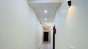 Un pasillo limpio y bien iluminado con suelo de baldosas, un extintor y una lámpara fijada a la pared.