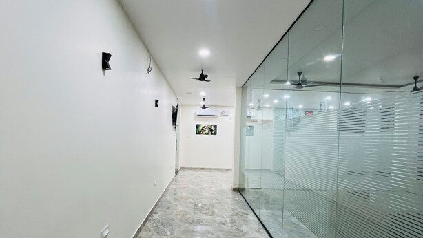 Un pasillo con piso de mármol, ventiladores de techo, iluminación empotrada y un panel de vidrio en un lateral.