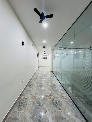 A hallway with a marble floor, ceiling fans, recessed lighting, and a glass partition on one side.