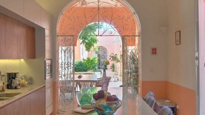 A kitchen with a central island, a dining area with chairs, and an archway leading to an outdoor patio. - CASA DE LOS PLATOS, IN THE HEART OF MÉRIDA (Centro)