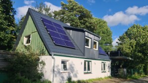 Une maison avec un toit en pente, des panneaux solaires et une petite fenêtre.