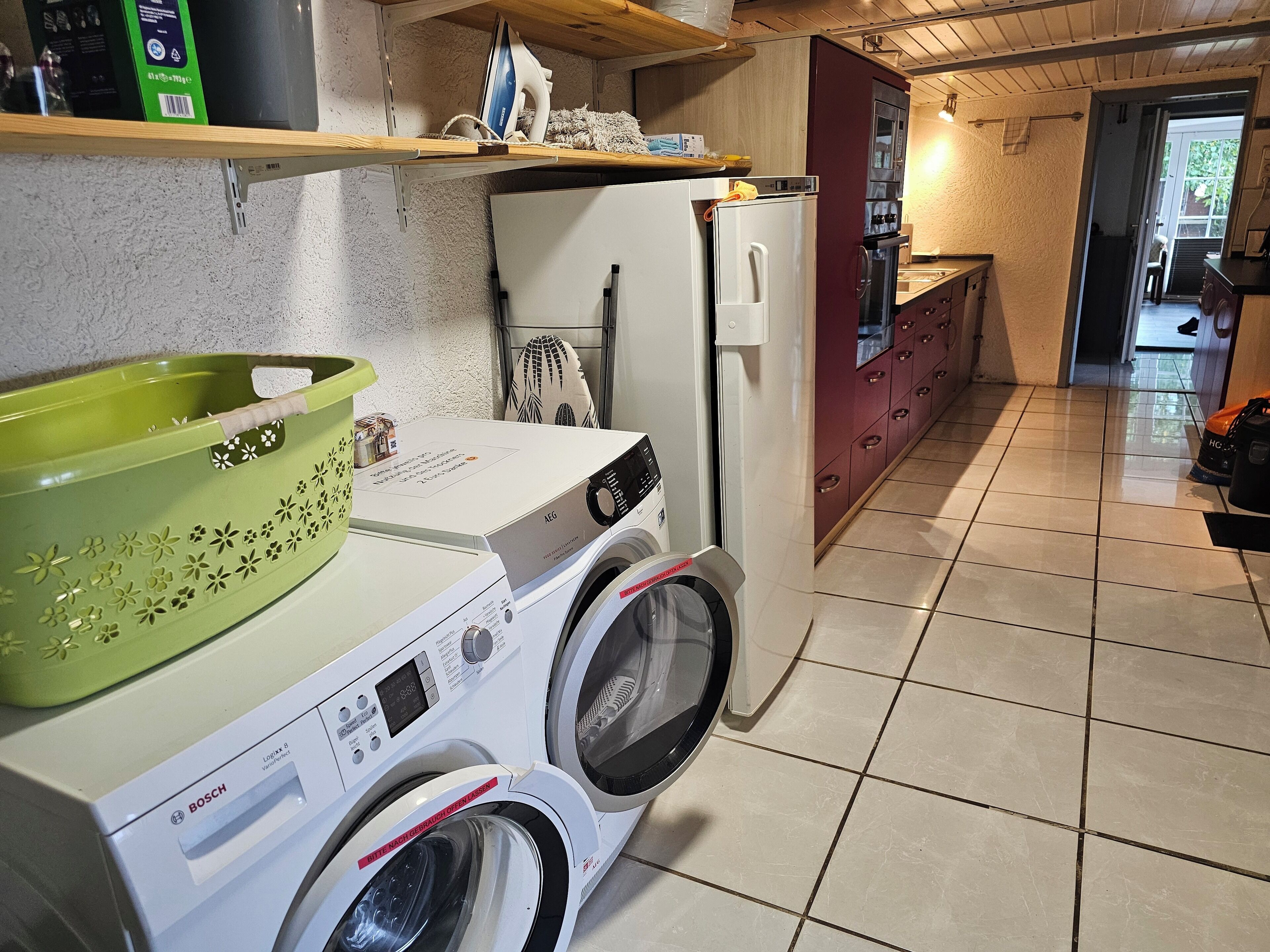 A compact kitchen with a washing machine, a refrigerator, and a shelf with various items.