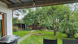 Un patio couvert comprenant un barbecue, une table et une chaise. Il y a un jardin avec un arbre et une balançoire.