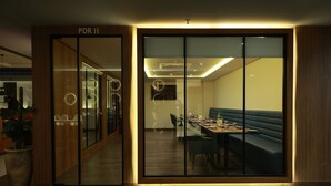 A modern dining area with a glass partition, a blue cushioned bench, and a long table set for dining. - Sangam Hotel By Sameeksha By Hospitality (Hyderabad)