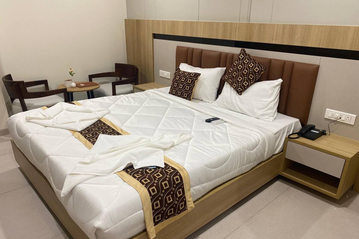 Een net opgemaakt bed met een gewatteerde witte dekbedovertrek, een houten hoofdbord en gestreepte kussens. Er staat een nachtkastje met een telefoon en een kleine lamp.