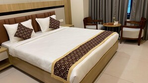 A neatly made bed with a patterned bedspread and pillows, a wooden headboard, and a small round table with chairs in a hotel room. - Sangam Hotel By Sameeksha By Hospitality (Hyderabad)