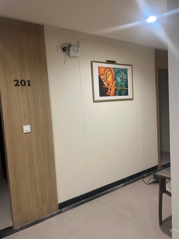 Un pasillo con una puerta de madera identificada con el número 201, una obra de arte enmarcada en la pared y una lámpara en el techo.