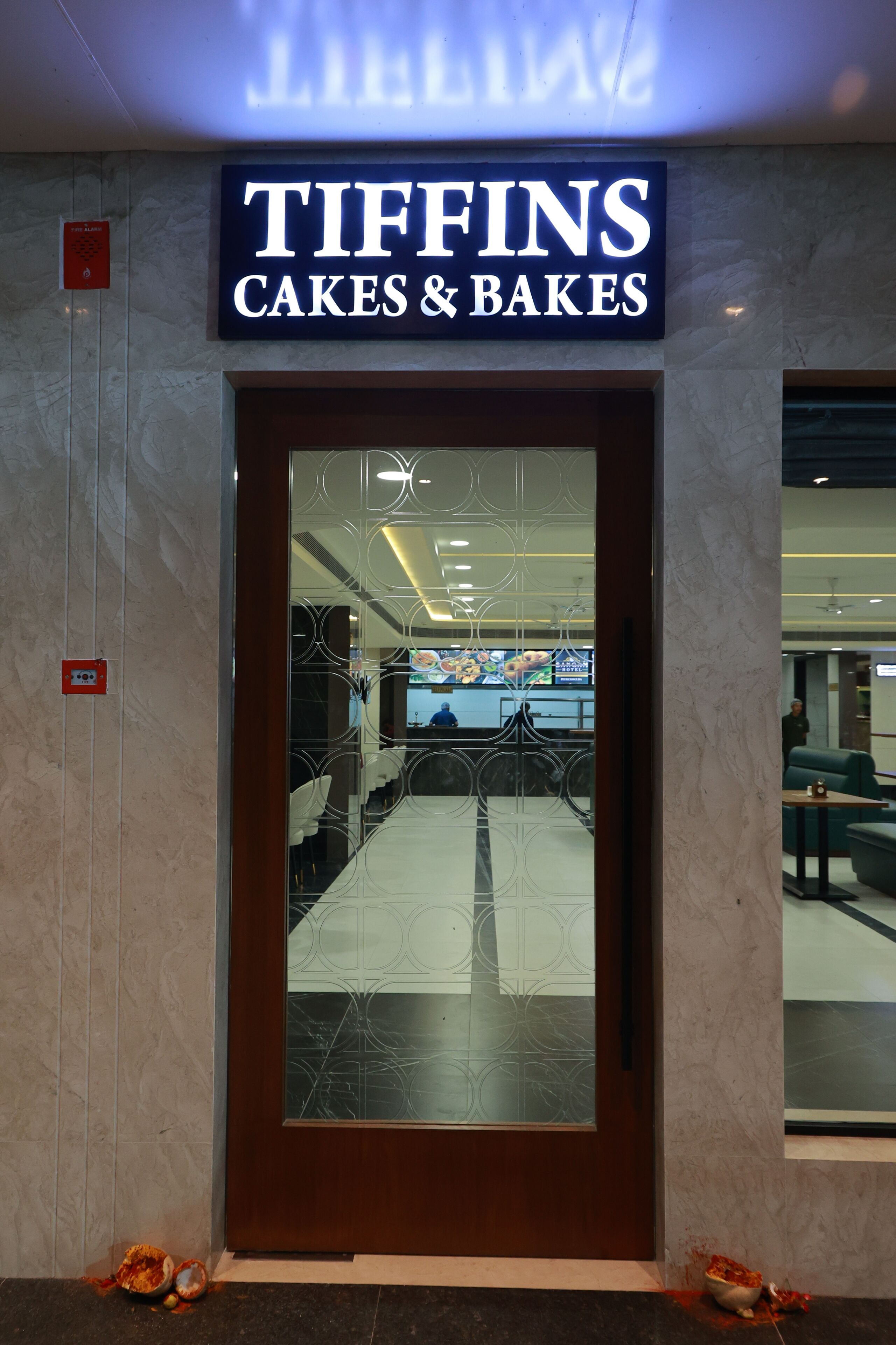 Un escaparate con un letrero que dice 'TIFFINS CAKES & BAKES' sobre una puerta con un panel de vidrio decorativo.