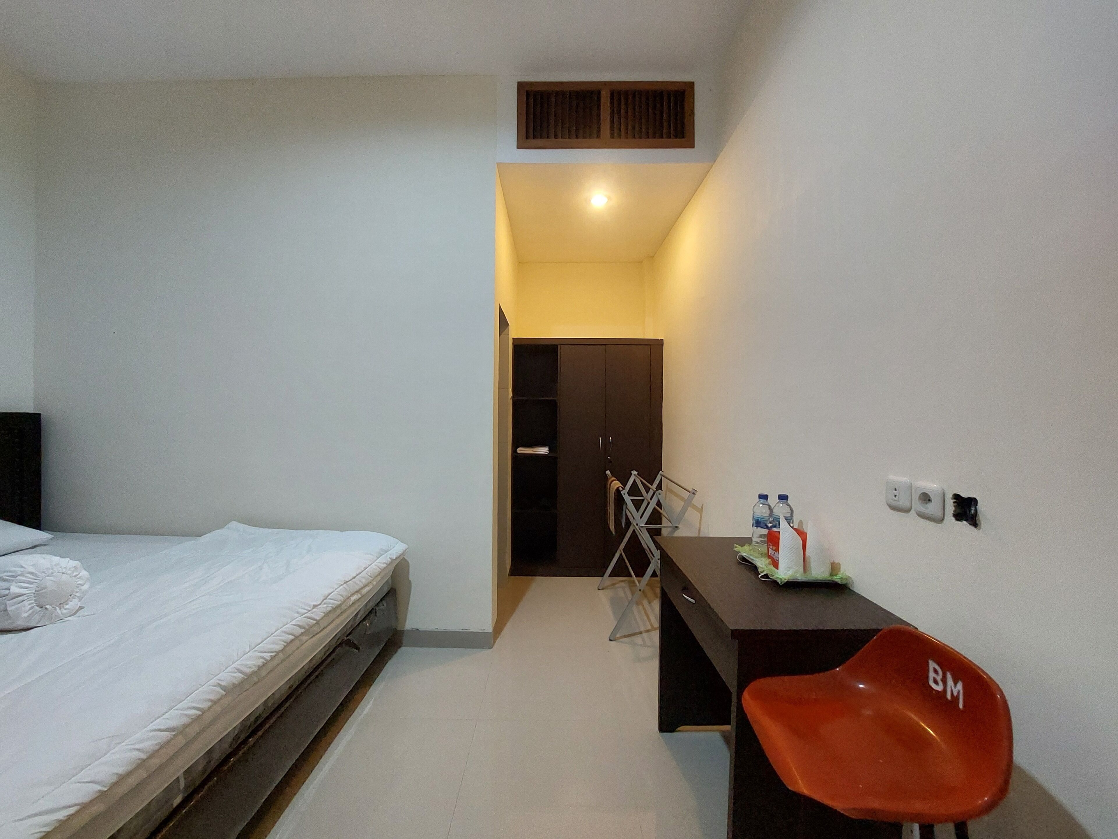 Une chambre à coucher comprenant un lit, un bureau avec une chaise, une armoire et une petite table sur laquelle sont posés divers objets.